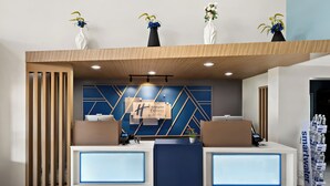 A hotel reception area with two reception desks, a geometric wall design, and three vases with flowers on top. - Holiday Inn Express & Suites Raleigh NE - Medical Ctr Area by IHG (Raleigh)