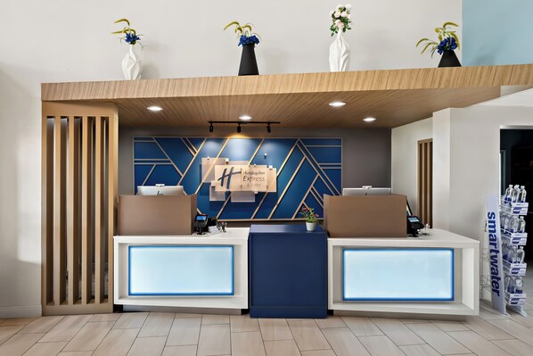 Een hotel receptie met twee balies, een geometrisch wandontwerp en drie vazen met bloemen.