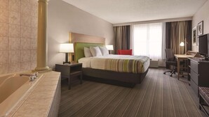 A hotel room with a large bed, a desk, a chair, a TV, a lamp, a nightstand, and a bathtub. - Country Inn & Suites by Radisson, Beaufort West, SC (Beaufort)