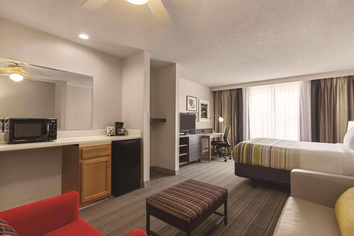 A hotel room with a bed, a desk with a computer, a microwave, and a small kitchenette.