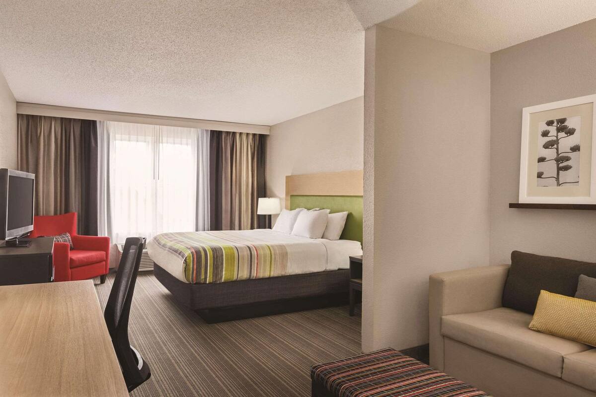 A hotel room with a bed, a desk with a chair, a sofa, and a television.