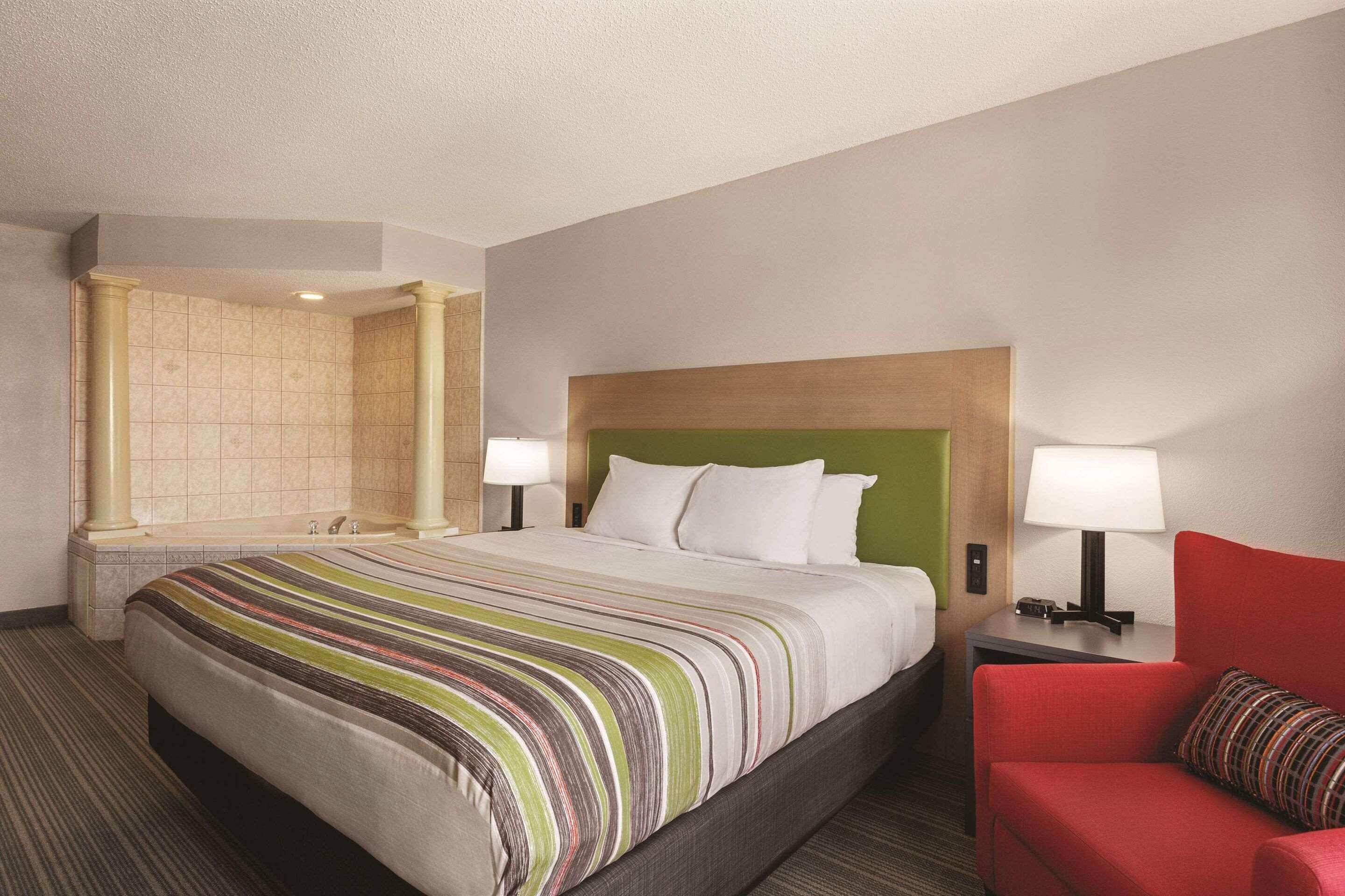 Une chambre d’hôtel avec un grand lit, un fauteuil rouge, une table de chevet avec une lampe et une tête de lit verte.