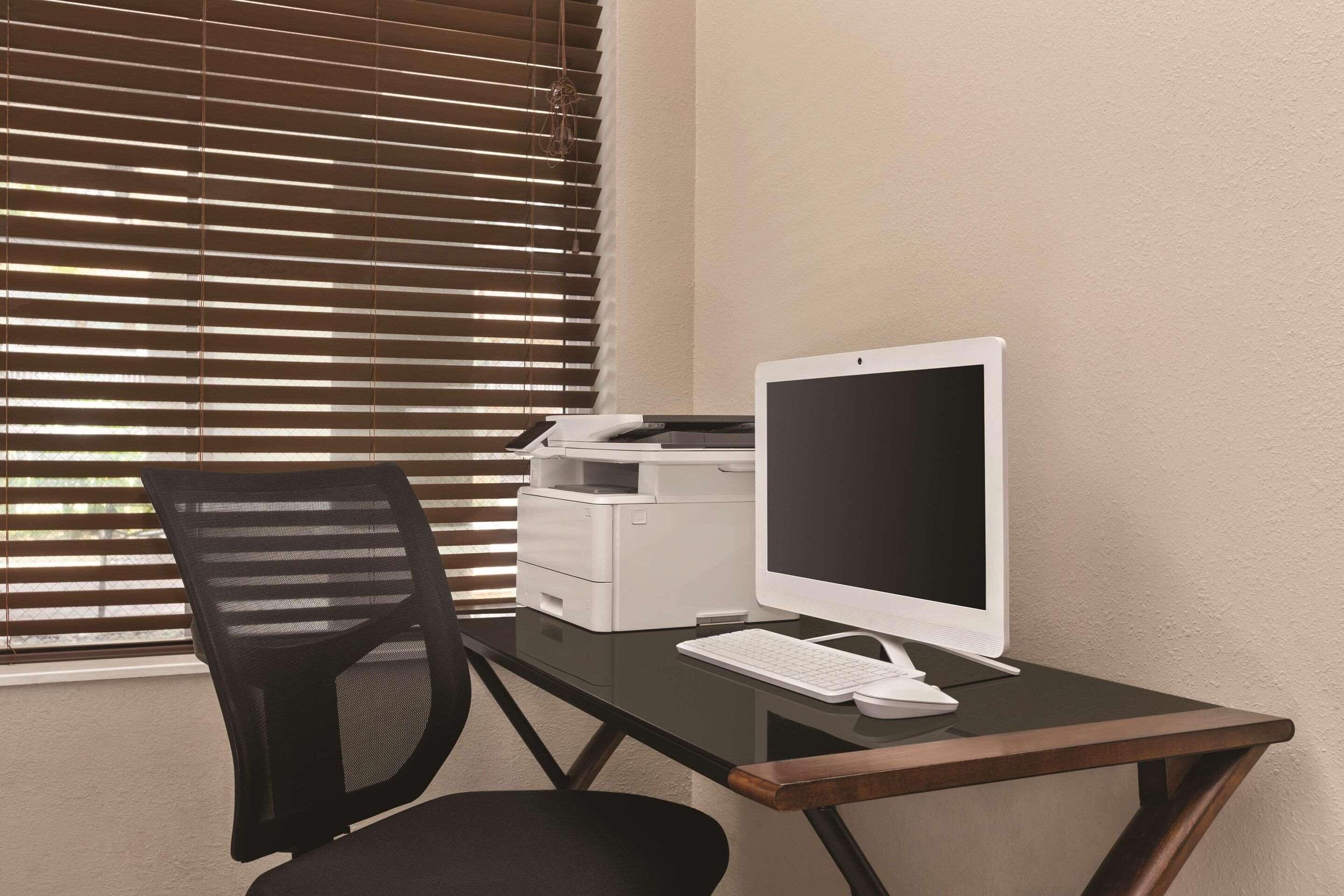 Un bureau avec un ordinateur de bureau, une imprimante et un fauteuil de bureau noir.