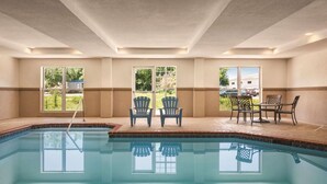 An indoor swimming pool with clear glass walls, two Adirondack chairs, and a table with chairs. - Country Inn & Suites by Radisson, Beaufort West, SC (Beaufort)