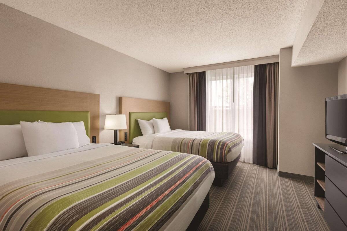 A hotel room with two beds, a television, and a window with curtains.