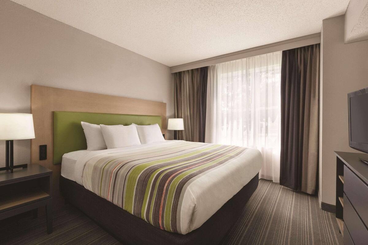 A hotel room with a large bed, two bedside tables, a TV, and a window with curtains.