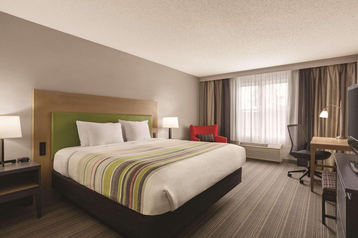 A hotel room with a large bed, a desk, a chair, and a TV.