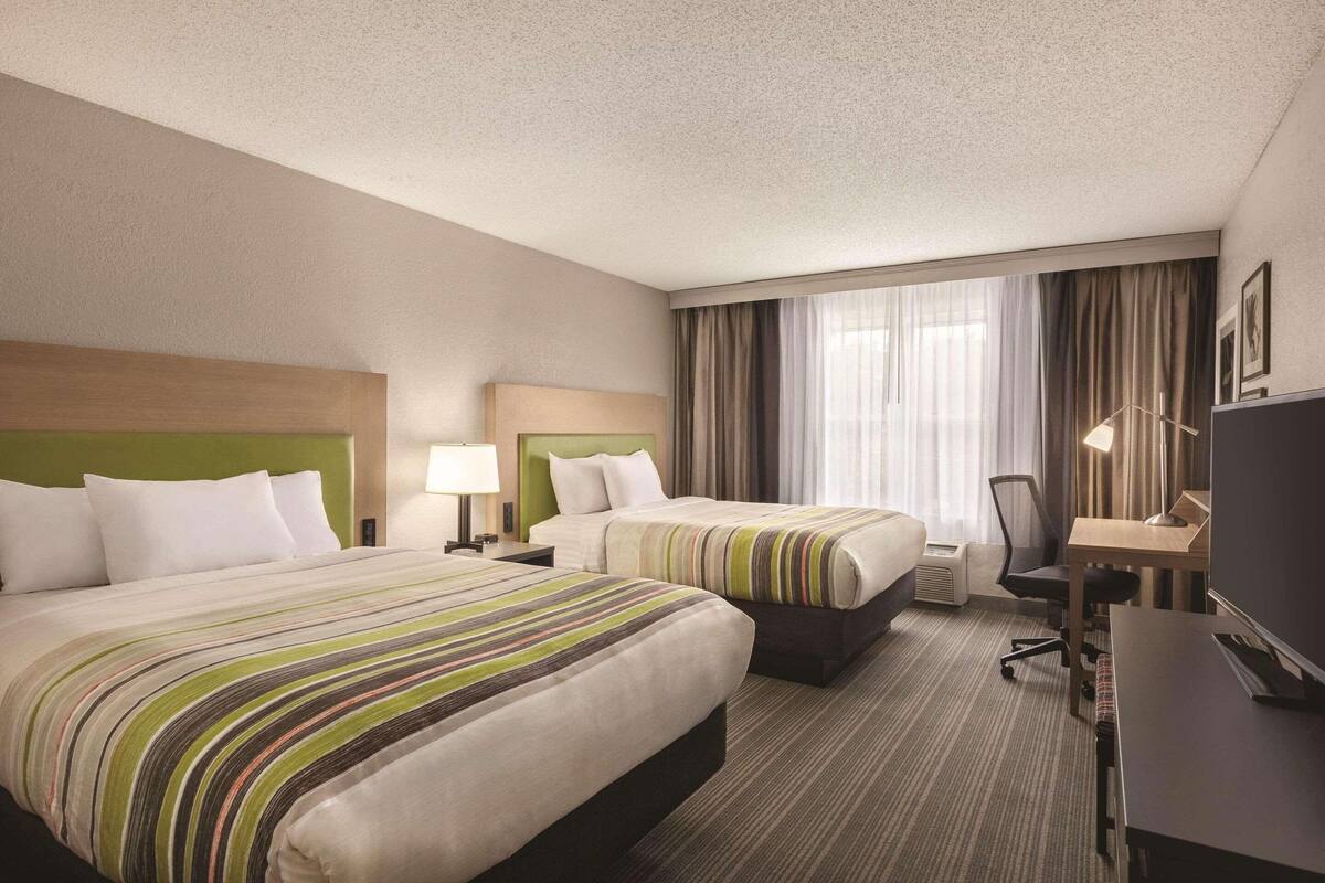A hotel room with two beds, a desk, a chair, a TV, and a window with curtains.