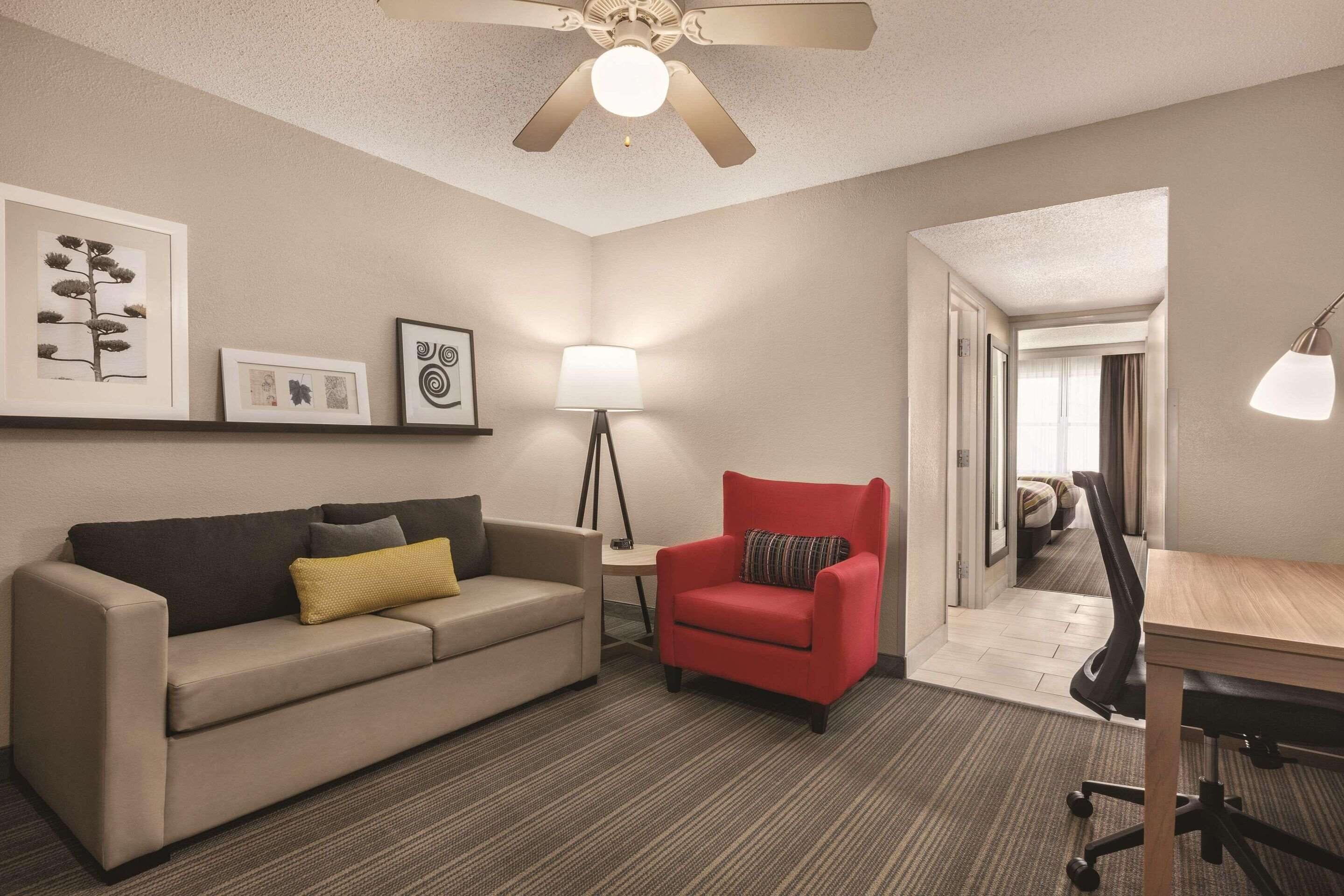A hotel room with a sofa, a red armchair, a desk, and a ceiling fan.