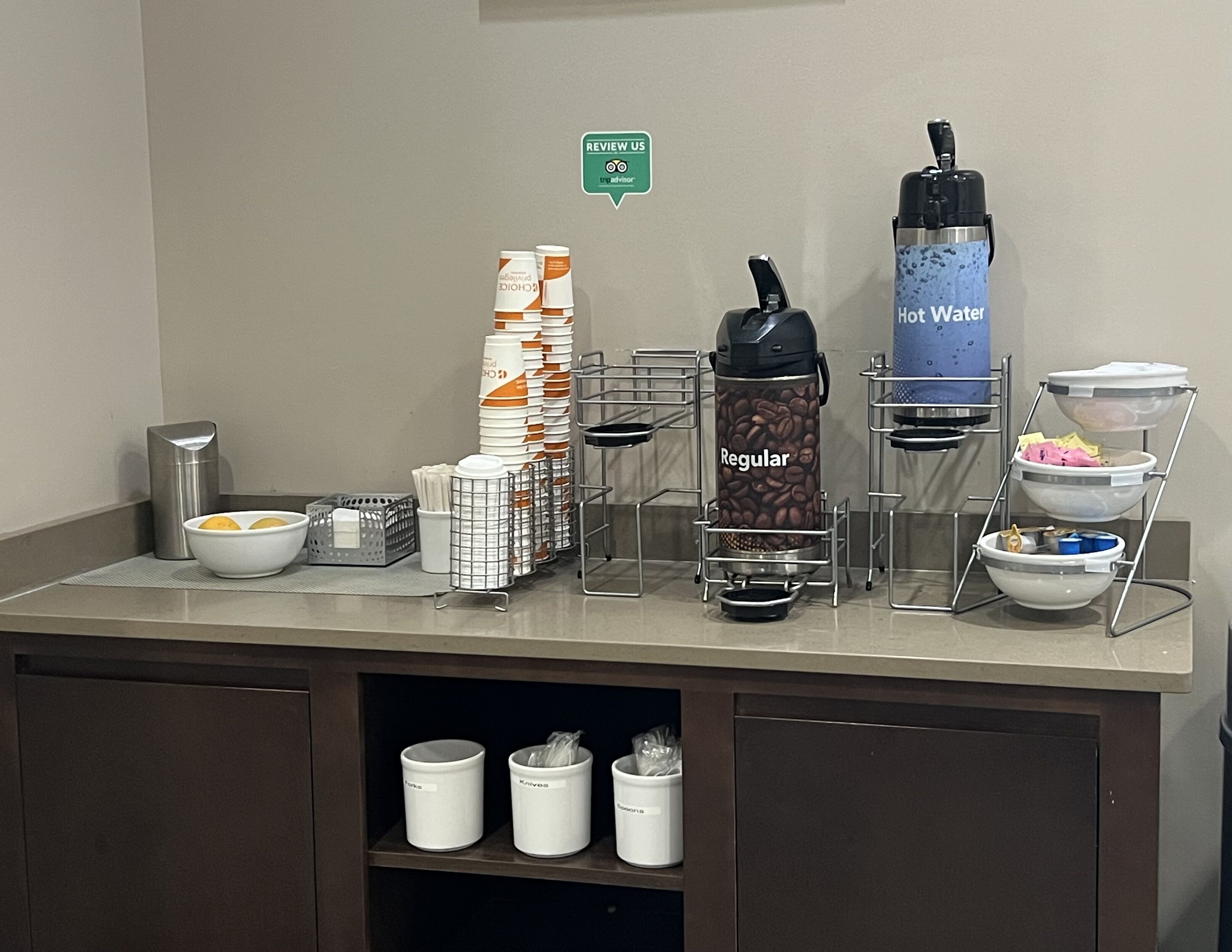 A self-service beverage station with hot and regular water dispensers, coffee, and tea options.