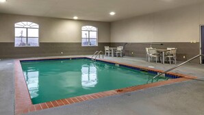 An indoor swimming pool with clear water, two windows with arched tops, and a seating area with chairs and a table.