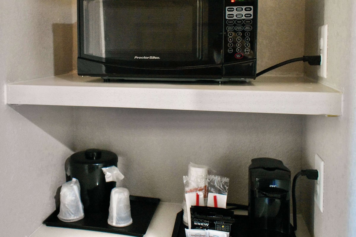 Un four à micro-ondes ProctorSillx sur une étagère blanche, une machine à café et un distributeur de capsules de café.