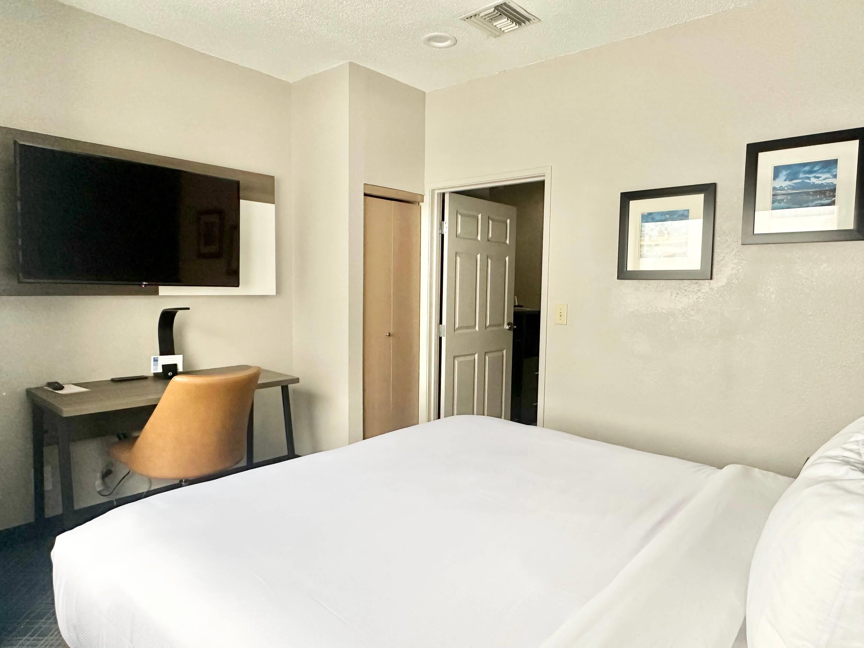 A hotel room with a bed, a desk, a chair, a television, and two framed pictures on the wall.