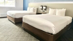 A hotel room with two beds, a large window, and a wall-mounted light fixture.