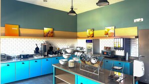 Een moderne keuken met blauwe kastjes, een roestvrijstalen aanrechtblad en diverse apparaten, waaronder een koffieapparaat en een broodmachine.