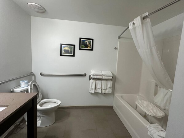A bathroom with a toilet, a sink, a bathtub with a shower curtain, and two framed pictures on the wall.