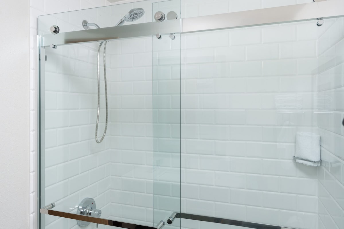 A glass-enclosed shower with a handheld showerhead and a towel rack.