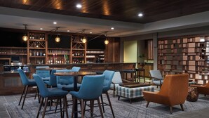 Un área de bar moderna con una mesa redonda, sillas azules y una variedad de botellas y vasos en estantes.