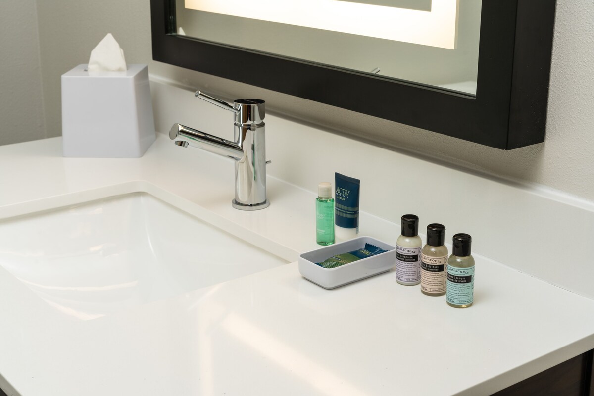 A bathroom sink with a tissue box, a mirror, and four toiletry bottles.