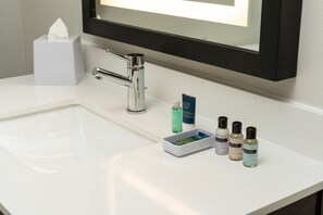 A bathroom sink with a tissue box, a mirror, and four toiletry bottles. - Four Points by Sheraton Chicago Schaumburg (Schaumburg)