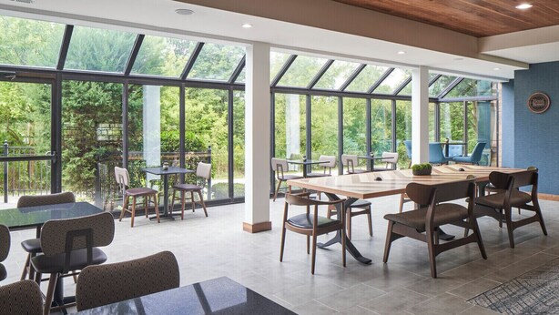 Un espacio interior amplio con ventanas grandes, una mesa de madera y varias sillas.