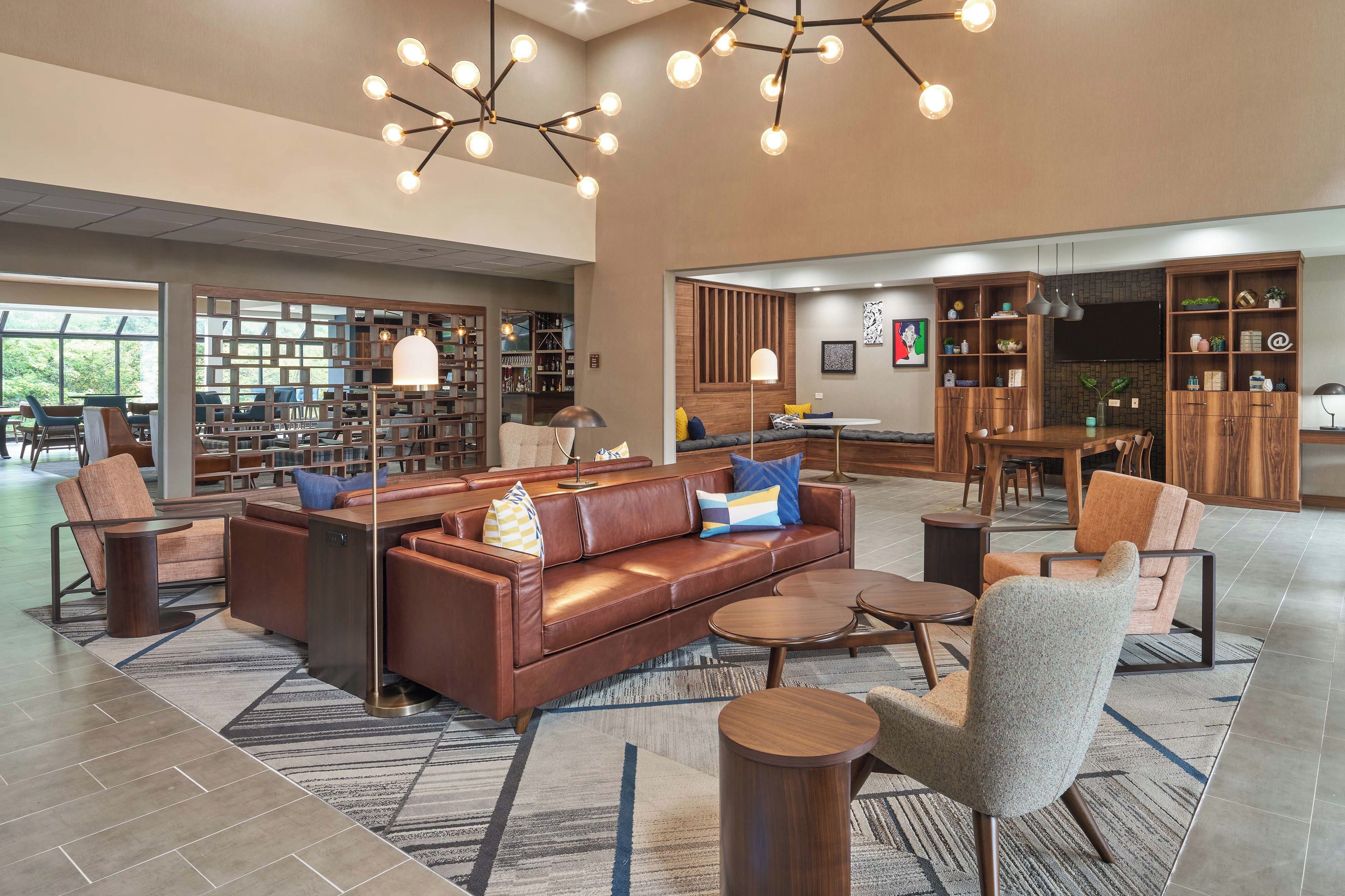 Een ruime lobby met een leren bank, fauteuils, een bijzettafeltje en een boekenplank.