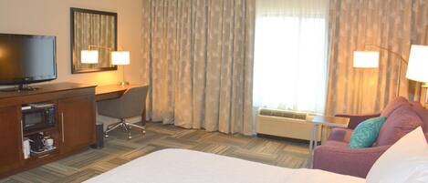 A hotel room with a large bed, a desk with a television, a chair, and two lamps.