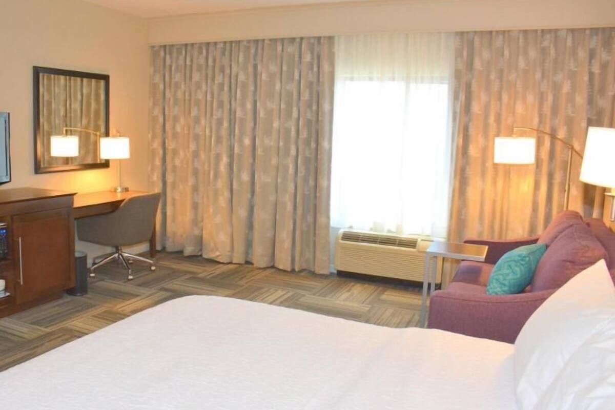 A hotel room with a large bed, a desk, a chair, a couch, and a lamp.