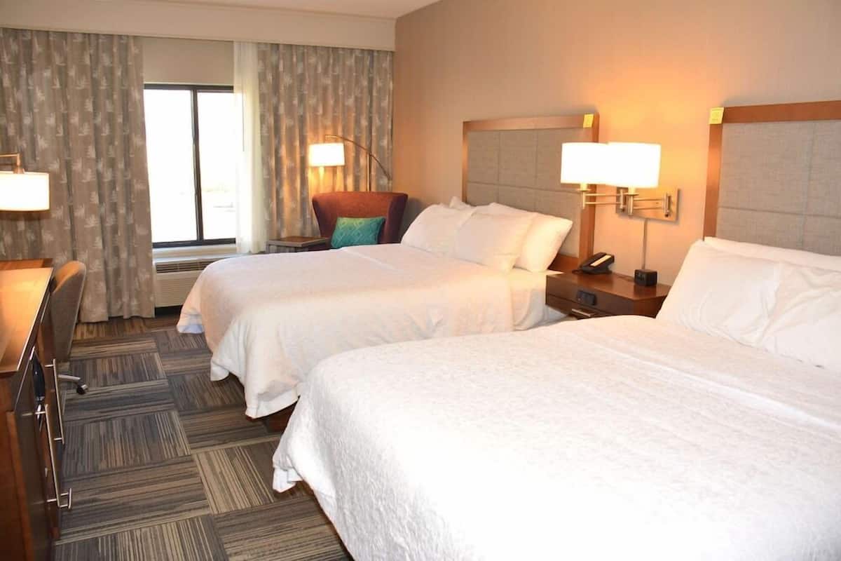 A hotel room with two beds, a desk, a chair, a lamp, and a window with curtains.