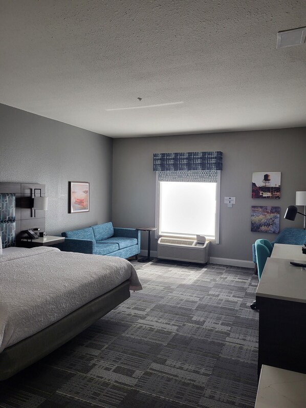 Une chambre d’hôtel avec un grand lit, un canapé bleu, un bureau et une fenêtre donnant sur des immeubles.