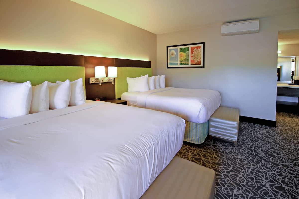 A hotel room with two beds, a nightstand with lamps, a small table, and a mirror.