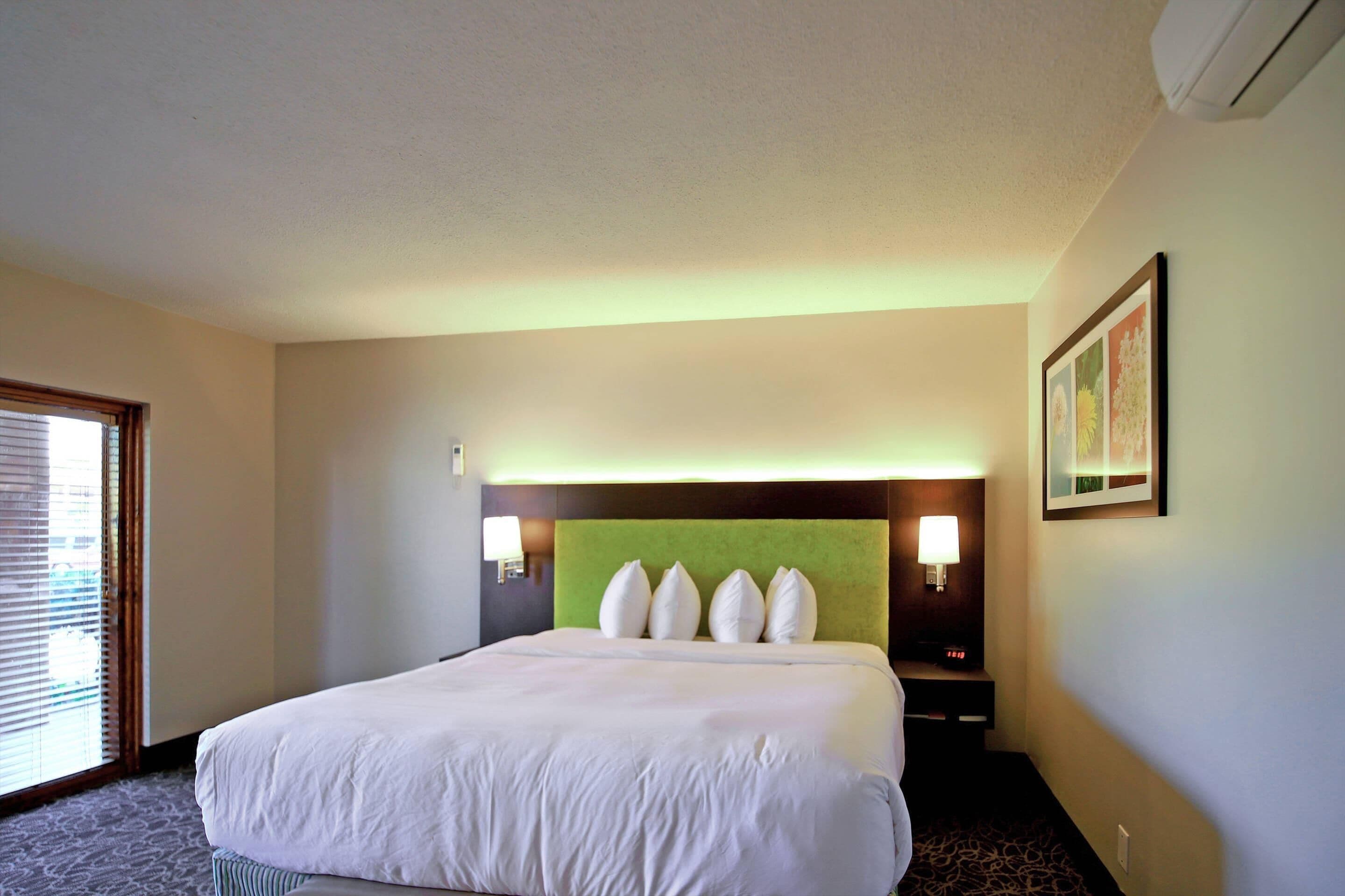 A hotel room with a large bed, a green headboard, two bedside lamps, and a framed picture on the wall.