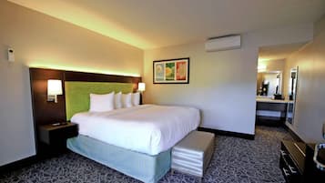 Ein Hotelzimmer mit einem großen Bett, Nachttischen, einem Kopfteil, einer Wand-Klimaanlage und einem kleinen Schreibtisch mit einer Lampe.