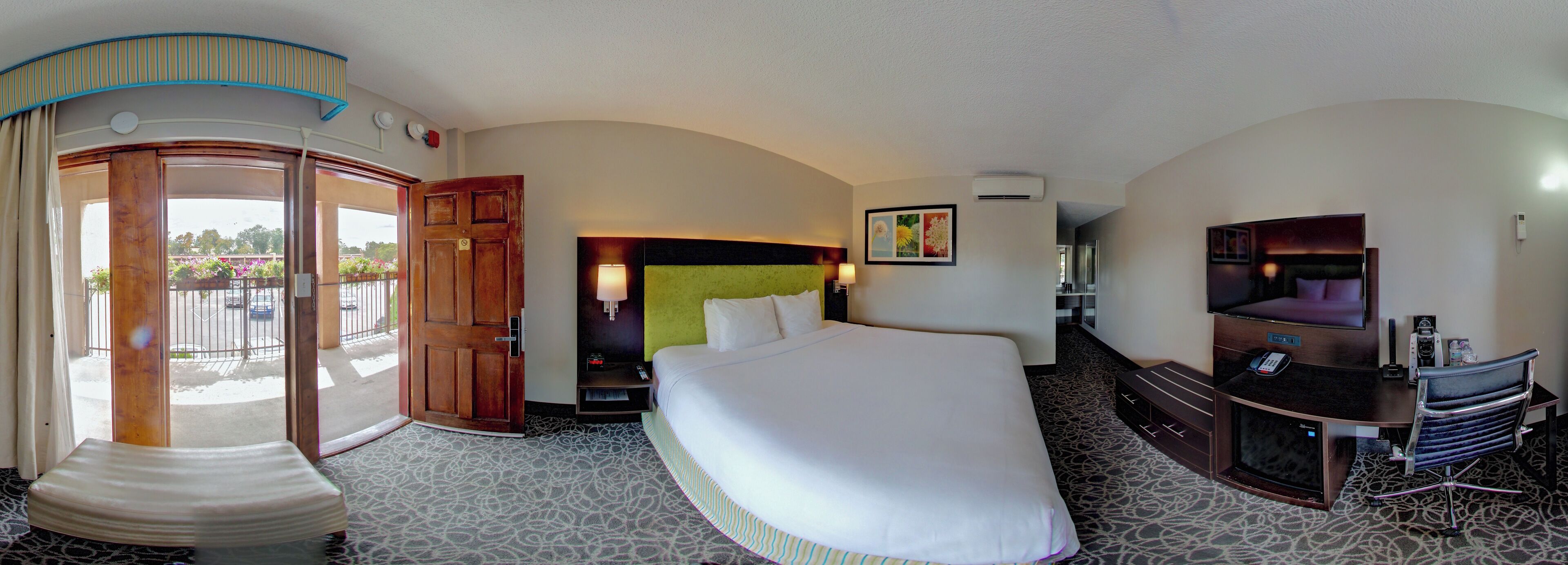 Une chambre d’hôtel avec un grand lit, une télévision, un bureau avec une chaise, une porte donnant sur l’extérieur et un climatiseur fixé au mur.