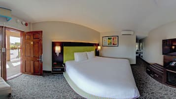 Een hotelkamer met een groot bed, een televisie, een bureau met stoel, een deur naar buiten en een wandairconditioner.
