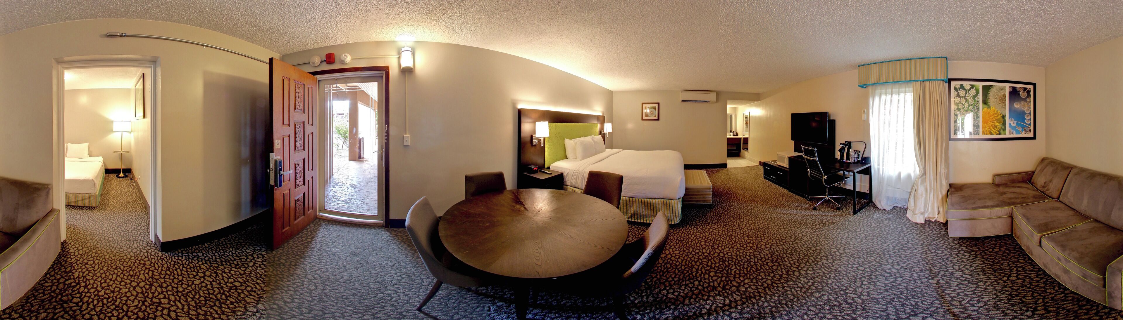 A hotel room with a bed, a dining table, a sofa, and a TV.