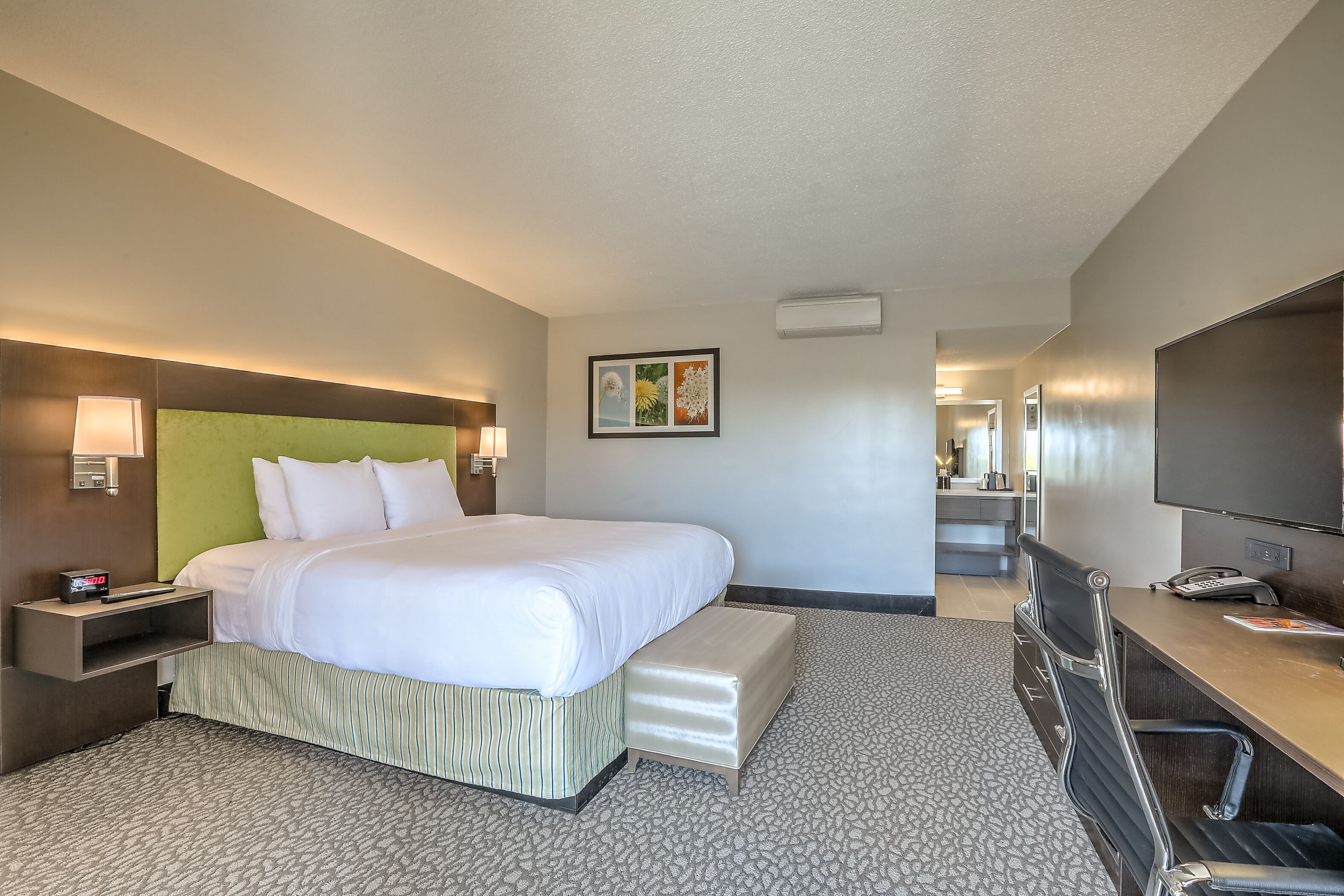 Une chambre d’hôtel avec un grand lit, un bureau, une chaise, une télévision et une salle de bain visible au fond.