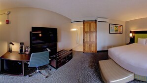 A hotel room with a bed, a desk with a TV, a bench, a door leading outside, and a wall-mounted air conditioner.