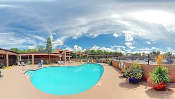 A swimming pool with lounge chairs and umbrellas, surrounded by a building with multiple windows and a covered patio area.