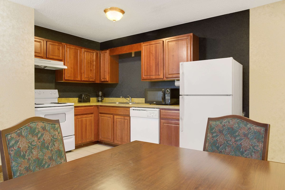 A kitchen with wooden cabinets, a white stove, a microwave, a dishwasher, and a dining table with chairs.