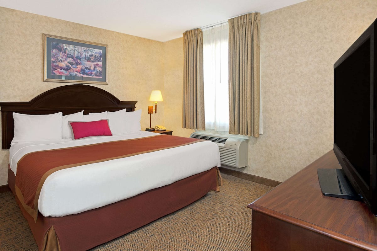 A hotel room with a large bed, a flat-screen TV, a desk, and a window with curtains.