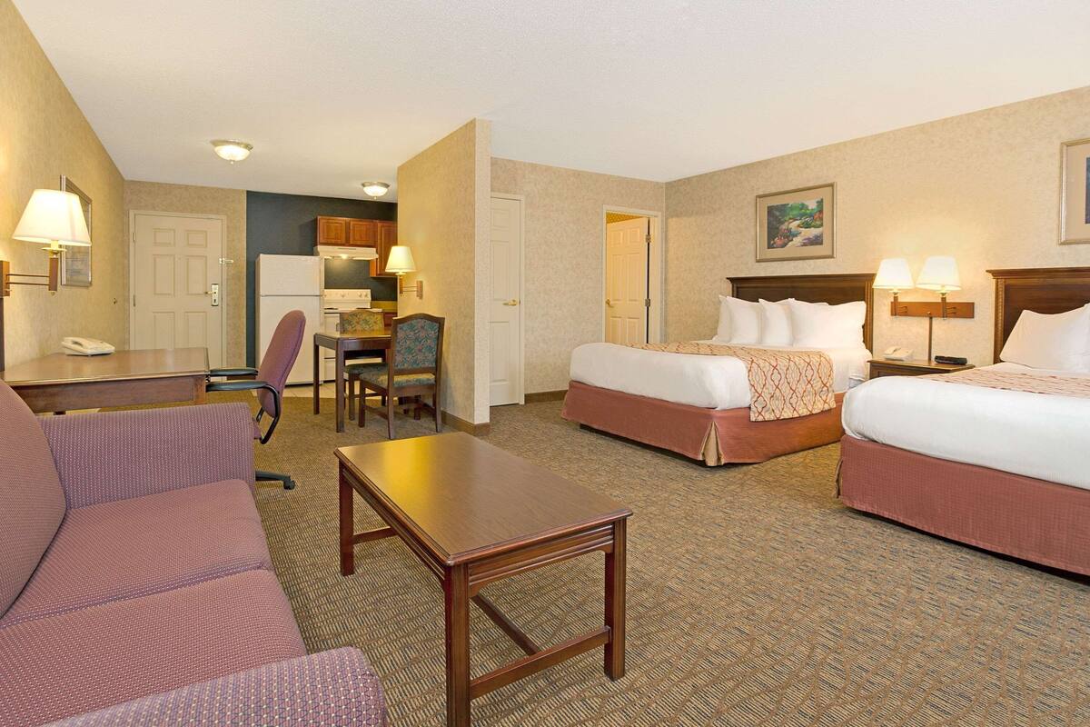 A hotel room with two beds, a desk, a chair, a sofa, and a kitchenette.
