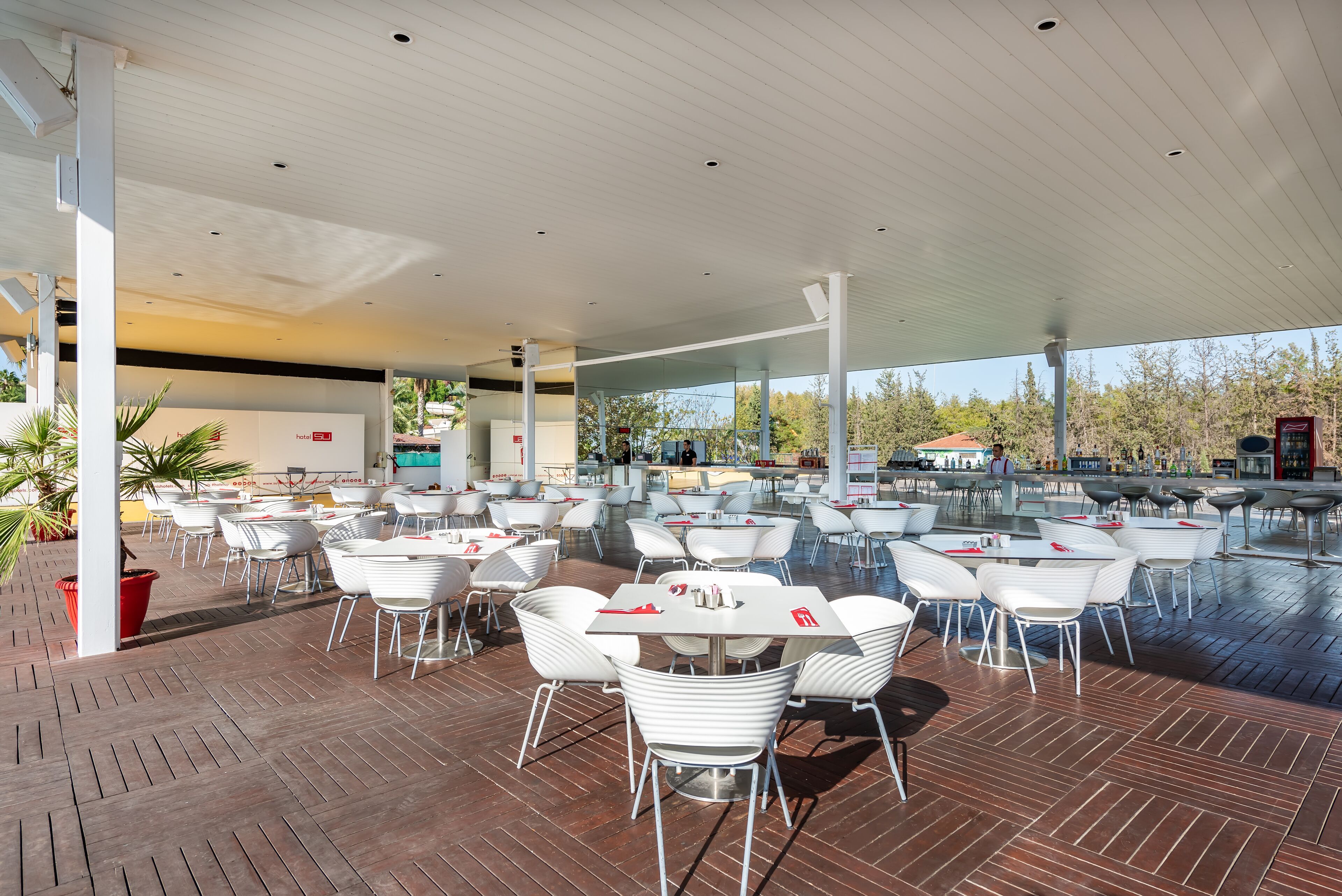 An outdoor dining area with white tables and chairs, a wooden deck, and a covered section with a bar area.