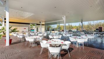 An outdoor dining area with white tables and chairs, a wooden deck, and a covered section with a bar area.
