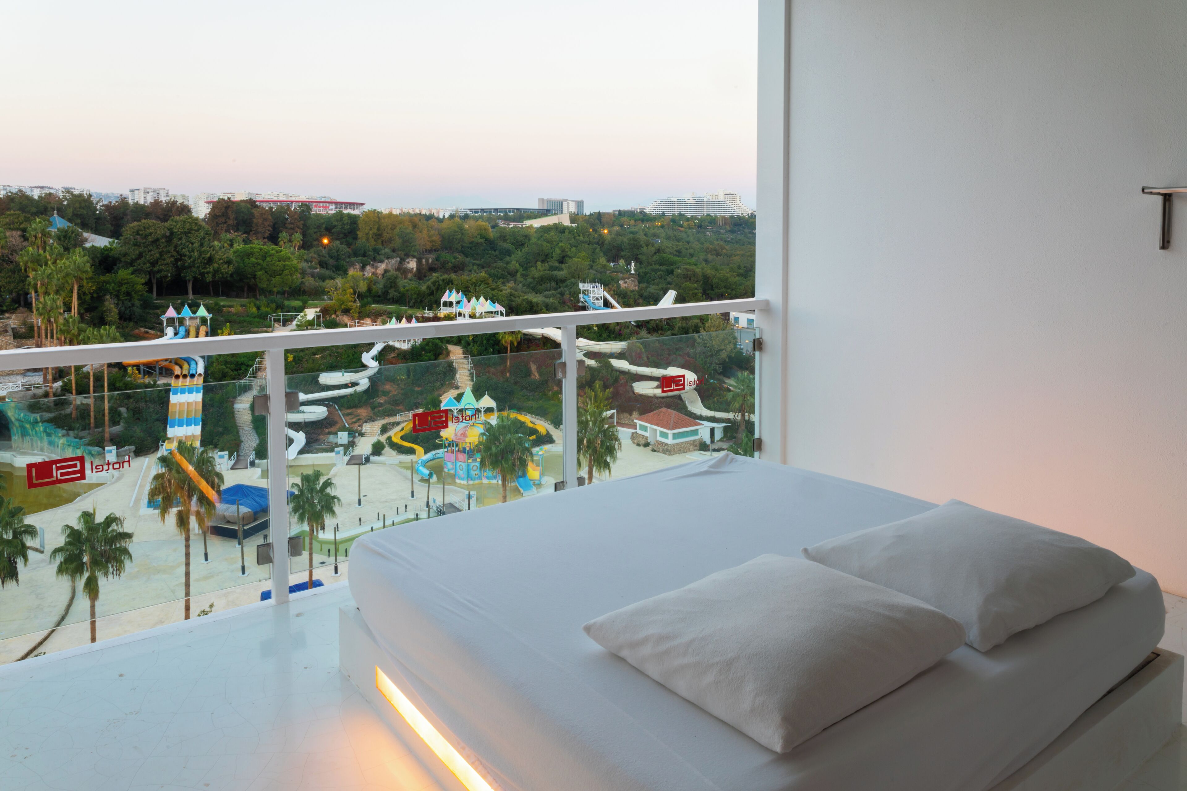 A hotel room with a balcony overlooking a water park and a cityscape.