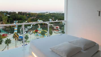 A hotel room with a balcony overlooking a water park and a cityscape.