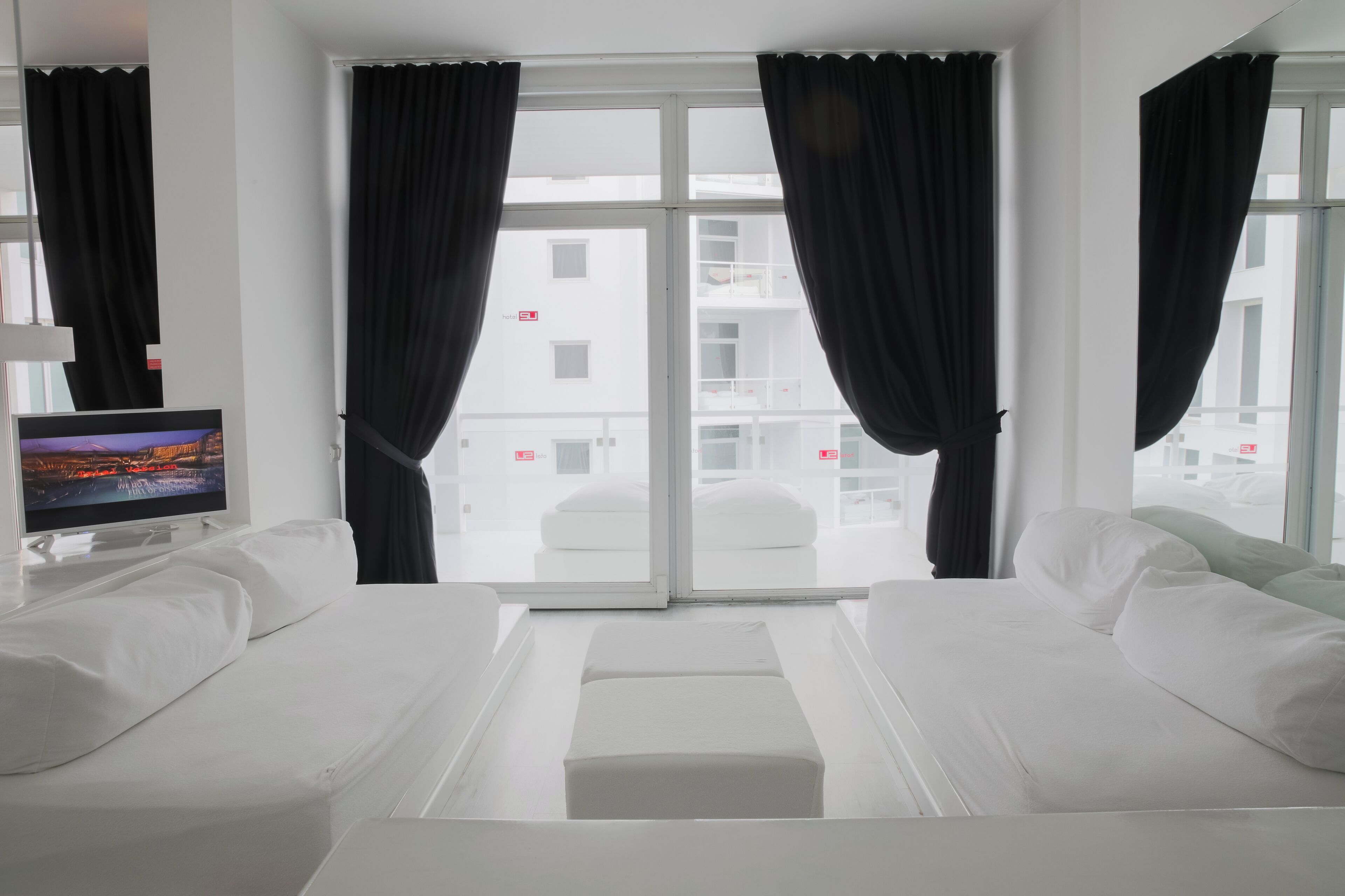 A hotel room with a bed, a TV, and a view of the outside.