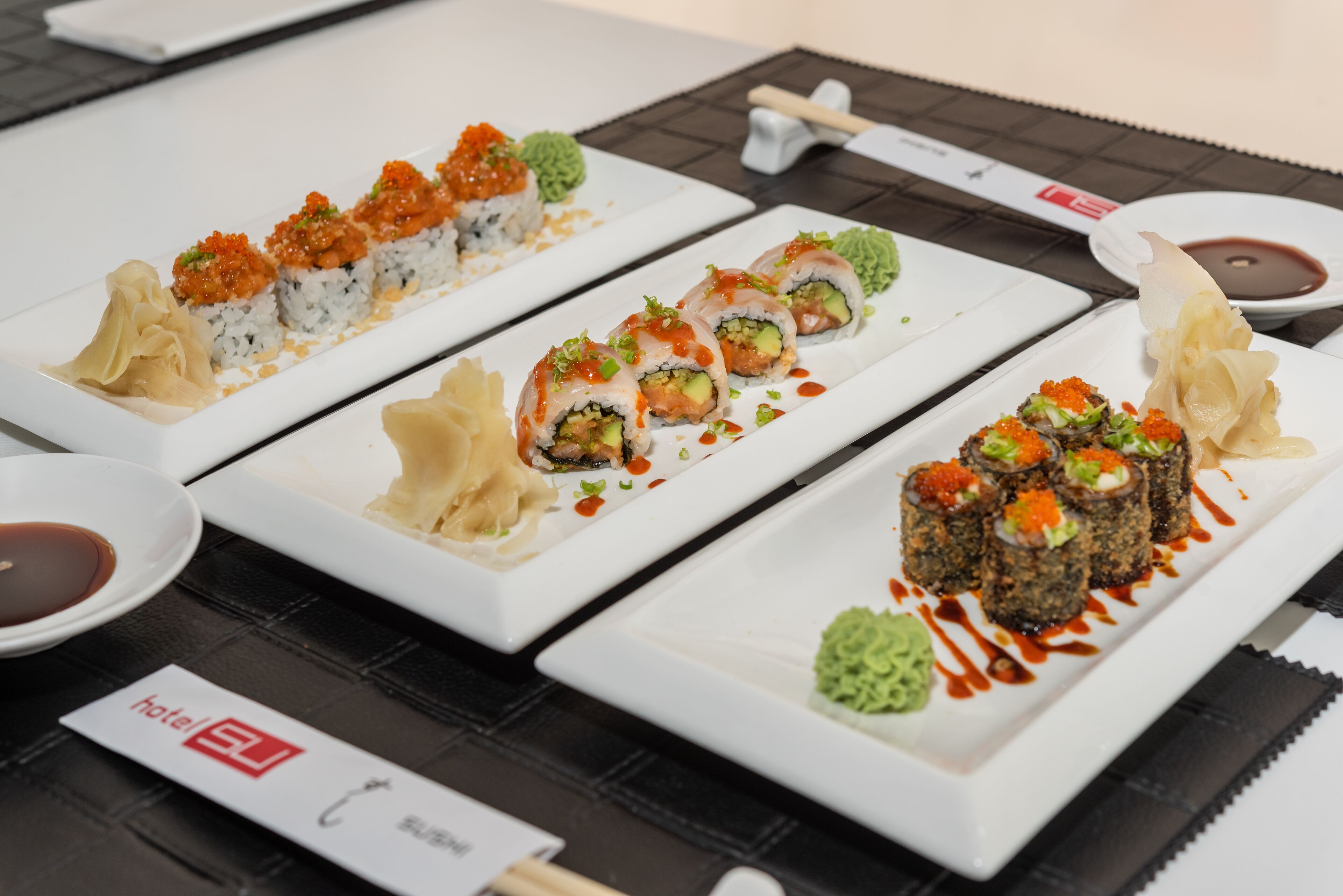 Ein Sushi-Teller mit verschiedenen Sushi-Sorten auf weißen Tellern, dazu kleine Schälchen mit Soßen und Wasabi.