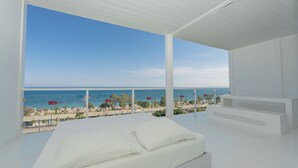 A modern bedroom with a large bed, white walls, and a balcony overlooking the beach and ocean. - Hotel SU & Aqualand (Antalya)