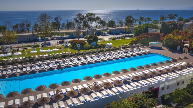 A large swimming pool with sun loungers and umbrellas, surrounded by greenery and buildings, with a view of the sea. - Hotel SU & Aqualand (Antalya)